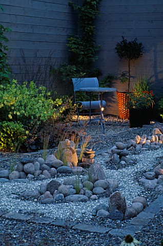 GARDEN_AT_NIGHT_REFLECTIVE_GRAVEL_RIVER_RUNS_AROUND_COBBLES_METAL_TABLE_AND_CHAIR_IN_BG_DESIGNER_HEI