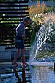 CHILD PLAYS IN FOUNTAIN IN MINIMALIST WATER GARDEN DESIGNED BY ULF NORDFJELL. HEDENS LUSTGARD  SWEDEN