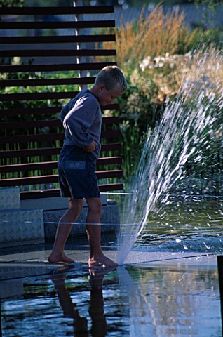 CHILD_PLAYS_IN_FOUNTAIN_IN_MINIMALIST_WATER_GARDEN_DESIGNED_BY_ULF_NORDFJELL_HEDENS_LUSTGARD__SWEDEN