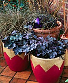 TERRACOTTA POTS ON TERRACOTTA PATIO PAINTED GOLD AND RED PLANTED WITH HEUCHERA QUICKSILVER   AJUGA BRAUNHERZ AND LARGE PURPLE BAUBLE.