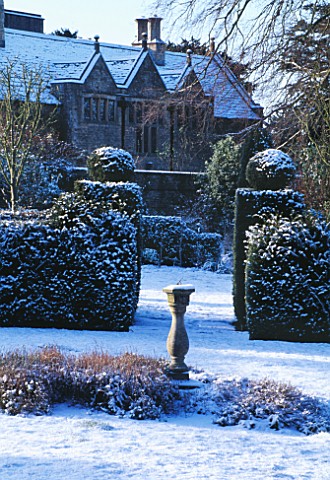 EASTLEACH_HOUSE__GLOUCS__COVERED_IN_SNOW__VIEWED_FROM_THE_WALLED_GARDEN_WITH_YEW_HEDGING_AND_A_SUNDI