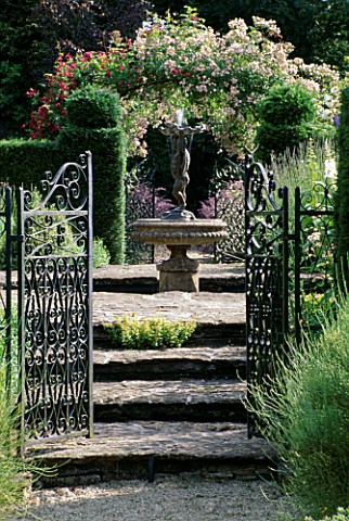 EASTLEACH_HOUSE_GARDEN__GLOUCESTERSHIRE_GATES__YEW_HEDGES__FOUNTAIN_AND_ROSE_ARCH_IN_THE_WALLED_GARD