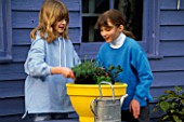HAZEL AND HANNAH PLANTING THE DECORATIVE HERB POT WITH  ROSEMARY BAY  MARJORAM AND PARSLEY