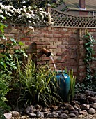 GRAVEL COURTYARD WITH WATER FEATURE: BRICK WALL  TRELLIS  WATER SPOUT   TURQUOISE CONTAINER  ROCKS AND CLEMATIS MONTANA