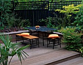 BELAU DECK TERRACE WITH BLACK MARBLE TABLE AND CHAIRS  ORANGE CUSHIONS  BLACK FENCE AND TRELLIS  ROBINIA AND NANDINA DOMESTICA. DESIGNER: SARAH LAYTON
