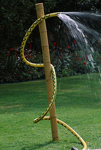 WATER_FEATURE_WATER_SERPENT_MADE_FROM_YELLOW_HOSE_TIED_WITH_TWINE_TO_BAMBOO_POLE_IN_LAWN_DESIGNER_CL