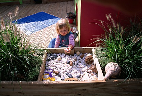 CHILDRENS_DECK_GARDEN_LUCY_FEELING_THE_SHELLS__FIR_CONES_AND_STONES_IN_A_RAISED_WOODEN_BED