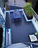 ROOF GARDEN DESIGNED BY STEPHEN WOODHAMS: BLACK SLATE TERRACE WITH METAL TABLE AND CHAIRS AND WATER FEATURE. NEON STRIP LIGHTING. GARDEN DESIGNED BY STEPHEN WOODHAMS.