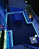 ROOF GARDEN DESIGNED BY STEPHEN WOODHAMS: BLACK SLATE TERRACE WITH METAL TABLE AND CHAIRS AND WATER FEATURE. NEON STRIP LIGHTING. GARDEN DESIGNED BY STEPHEN WOODHAMS