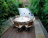 ROOF TERRACE WITH DECKING  WOODEN TABLE AND CHAIRS  GALVANISED METAL CONTAINERS WITH BAMBOO  WHITEWASHED WALL :DESIGNED BY WYNNIATT-HUSEY CLARKE