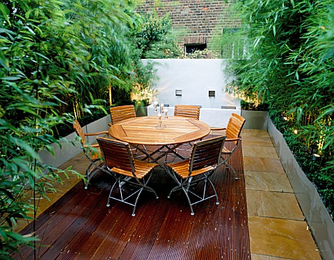 ROOF_TERRACE_WITH_DECKING_AT_NIGHT__WOODEN_TABLE_AND_CHAIRS__GALVANISED_METAL_CONTAINERS_WITH_BAMBOO