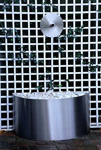 WATER_FEATURE_STAINLESS_STEEL_DISC_AND_SPOUT_POURS_INTO_A_STAINLESS_STEEL_CONTAINER_WITH_WHITE_PEBBL