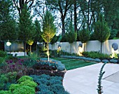 THE SANCTUARY GARDEN  CHELSEA 2002  LIT UP AT NIGHT. DESIGNER: STEPHEN WOODHAMS: LIMESTONE TERRACE  LAWN  CLIPPED CARPINUS BETULUS  WATER FEATURE. 5 FACE SCULPTURE BY STEPHEN COX