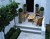 A PLACE TO SIT: TABLE AND CHAIRS  ICE WHITE SAWN GRANITE SETTS  EARTHENWARE POTS PLANTED WITH BOX BALLS  ESPALIERED PYRUS CALLERYANA CHAUNTICLEER. DESIGN/CHARLOTTE SANDERSON