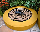 RAISED CHILDRENS SANDPIT PAINTED MUSTARD YELLOW WITH METAL SPIDERS WEB GRID OVER THE TOP. MERCEDES - BENZ GARDEN  TATTON PARK 2002. DESIGNED BY JANE MOONEY