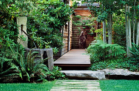 VIEW_ALONG_FRONT_WOODEN_PATH_WITH_LAWN__STONE_WATER_FEATURE_WITH_COPPER_PIPE__ROCK__DECKING_AND_ASPE