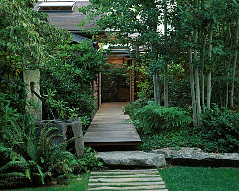VIEW_ALONG_FRONT_WOODEN_PATH_WITH_LAWN__STONE_WATER_FEATURE_WITH_COPPER_PIPE__ROCK__DECKING_AND_ASPE