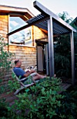 BOB SWAIN RELAXES ON THE DECK OUTSIDE THE HOUSE WITH THE OUTDOOR SHOWER ON THE RIGHT. DESIGNER BOB SWAIN  SEATTLE  USA