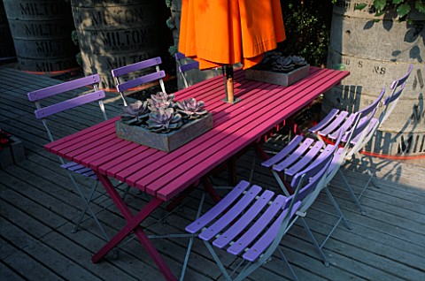 BLUE_CAFE_CHAIRS__PINK_WOODEN_TABLE__ORANGE_PARASOL__DECKING_AND_GALVANISED_TRAY_PLANTED_WITH_SUCCUL