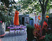 VIEW TOWARDS FLAT WITH BLUE CAFE CHAIRS  PINK WOODEN TABLE  ORANGE PARASOL  DECKING  ORANGE CANNAS AND GALVANISED TRAY PLANTED WITH SUCCULENTS: DESIGNER: STEPHEN WOODHAMS