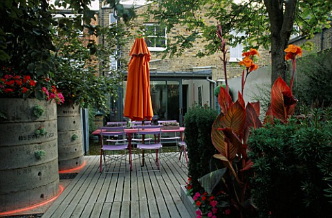 VIEW_TOWARDS_FLAT_WITH_BLUE_CAFE_CHAIRS__PINK_WOODEN_TABLE__ORANGE_PARASOL__DECKING__ORANGE_CANNAS_A