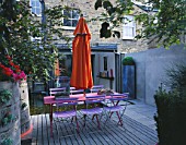 VIEW TOWARDS FLAT WITH BLUE CAFE CHAIRS  PINK WOODEN TABLE  ORANGE PARASOL  DECKING AND ORANGE CANNAS : DESIGNER: STEPHEN WOODHAMS