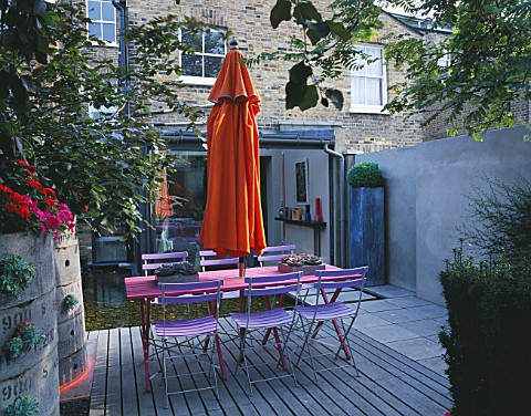 VIEW_TOWARDS_FLAT_WITH_BLUE_CAFE_CHAIRS__PINK_WOODEN_TABLE__ORANGE_PARASOL__DECKING_AND_ORANGE_CANNA