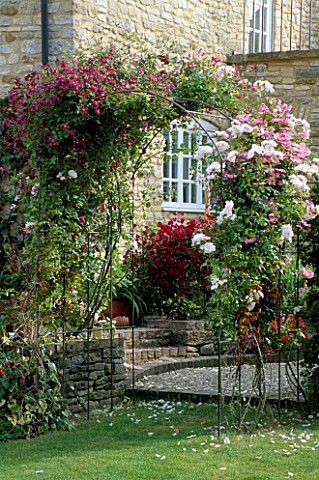 LAUNA_SLATTERS_GARDEN__OXFORDSHIRE_METAL_ROSE_PERGOLA_IN_FRONT_OF_THE_HOUSE_PLANTED_WITH_CLIMBING_RO