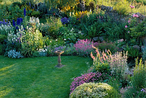 LAUNA_SLATTERS_GARDEN_OXFORDSHIRE_BORDER_BESIDE_POND_WITH_LAWN_AND_SUNDIAL__PLANTED_WITH_HEBE_RAKAIE