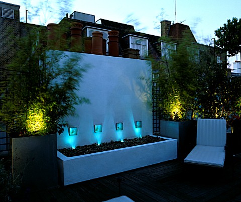 ROOF_GARDEN_LIT_UP_AT_NIGHT_WITH_DECKING__WHITE_WATER_FEATURE__CHAIRS_AND_GALVANISED_POTS_PLANTED_WI