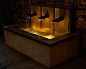 WATER FEATURE LIT UP AT NIGHT: RAISED WATER FEATURE WITH COPPER SPOUTS. DESIGNER: CLAIRE MEE
