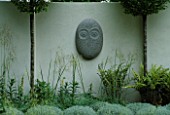 SANCTUARY GARDEN SPONSORED BY MERRILL LYNCH AT THE CHELSEA FLOWER SHOW 2002: DESIGNED BY STEPHEN WOODHAMS: ONE OF THE FIVE FACE SCULPTURES BY STEPHEN COX BESIDE CLIPPED SANTOLINA