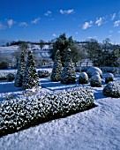 SNOW COVERS THE LOWER PARTERRE WITH BOX AND YEW SHAPES AND THE COUNTRYSIDE BEYOND. PETTIFERS GARDEN  OXFORDSHIRE