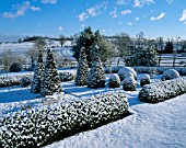 SNOW COVERS THE LOWER PARTERRE WITH BOX AND YEW SHAPES AND THE COUNTRYSIDE BEYOND. PETTIFERS GARDEN  OXFORDSHIRE