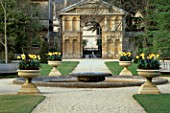 THE OXFORD BOTANIC GARDEN: POOL AND FOUNTAIN WITH STONE CONTAINERS PLANTED WITH TULIPS  PANSIES AND MUSCARI AND ENTRANCE GATEWAY BY NICHOLAS STONE BEHIND