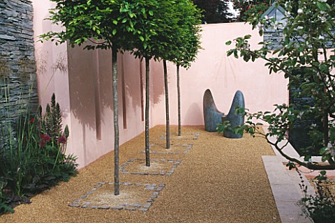 TWO_ROUNDED_METAL_SEATS_IN_FRONT_OF_PINK_WALLS_IN_LLADROS_SENSUALITY_GARDEN_ROW_OF_CLIPPED_CARPINUS_