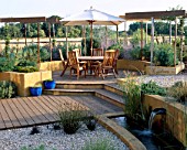 GRAVEL GARDEN WITH RENDERED CONCRETE WALL  POOL WITH SPOUT WATER FEATURE  DECKING PERGOLA  TABLE AND CHAIRS  CREAM PARASOL. DESIGNER: MARK LAURENCE