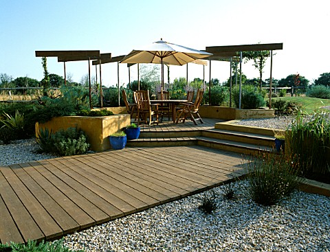 GRAVEL_GARDEN_WITH_RENDERED_CONCRETE_WALLS__DECKING__PERGOLA__TABLE_AND_CHAIRS__CREAM_PARASOL_DESIGN