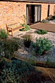 GRAVEL GARDEN BESIDE THE HOUSE WITH WOODEN BENCH AND STEPPING STONES. DESIGNER: MARK LAURENCE