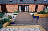 GRAVEL GARDEN BESIDE THE HOUSE WITH WOODEN BENCH  WOODEN DECKING  STEPPING STONES AND RENDERED CONCRETE WALL. DESIGNER: MARK LAURENCE