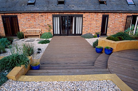 GRAVEL_GARDEN_BESIDE_THE_HOUSE_WITH_WOODEN_BENCH__WOODEN_DECKING__STEPPING_STONES_AND_RENDERED_CONCR
