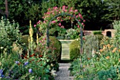 THE PRIORY  BEECH HILL  BERKSHIRE: THE HERBACEOUS BORDER WITH WOODEN ARCH PLANTED WITH AN AMERICAN PILLAR ROSE