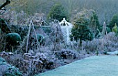WEST GREEN HOUSE GARDEN  HAMPSHIRE: FROSTY BORDER IN WINTER WITH SEDUMS AND WOODEN TRIPODS IN FRONT OF A WHITE ORNAMENTAL SEAT IN THE WALLED GARDEN