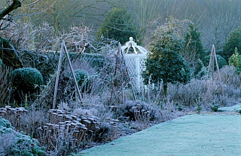 WEST_GREEN_HOUSE_GARDEN__HAMPSHIRE_FROSTY_BORDER_IN_WINTER_WITH_SEDUMS_AND_WOODEN_TRIPODS_IN_FRONT_O