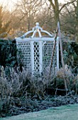 WEST GREEN HOUSE GARDEN  HAMPSHIRE: FROSTY BORDER IN WINTER WITH A WOODEN TRIPOD IN FRONT OF A WHITE ORNAMENTAL SEAT IN THE WALLED GARDEN