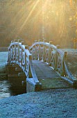WEST GREEN HOUSE GARDEN  HAMPSHIRE: EARLY MORNING SUNLIGHT STRIKES AN ORNAMENTAL BRIDGE ACROSS A LAKE IN THE NEO-CLASSICAL PARK GARDEN DESIGNED BY QUINLAN TERRY