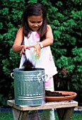 DESIGNER CLARE MATTHEWS: WORMERY PROJECT. GIRL TIPPING COMPOST INTO METAL DUSTBIN