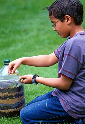 DESIGNER_CLARE_MATTHEWS__WORMERY_PROJECT__BOY_PUTS_GRASS_CUTTINGS_INTO_GLASS_JAR_WITH_PLASTIC_BOTTLE