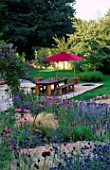 DESIGNER CLARE MATTHEWS: THE STONE TERRACE WITH GREEN OAK TABLE AND BENCHES AND RED PARASOL SEEN FROM THE WALLED GARDEN