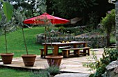 DESIGNER CLARE MATTHEWS: THE STONE TERRACE WITH GREEN OAK TABLE AND BENCHES  OLIVE TREES IN TERRACOTTA CONTAINERS AND A RED PARASOL